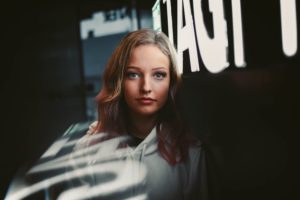 blond girl with hazel eyes in front of a neon sign